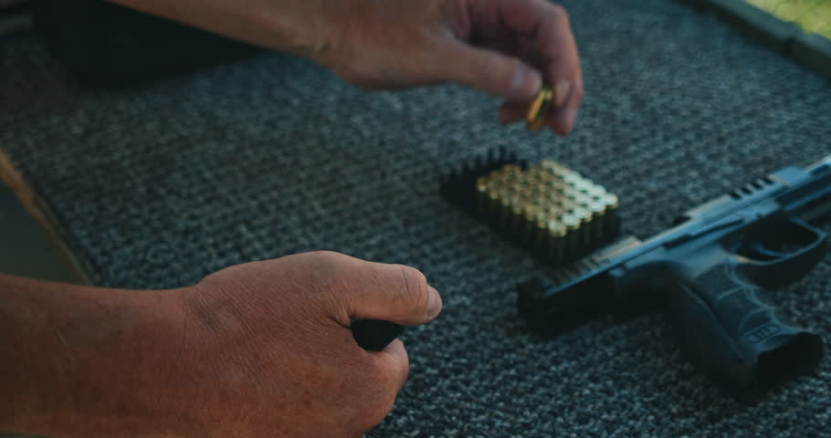 Loading bullets into pistol magazine on carpeted shooting table