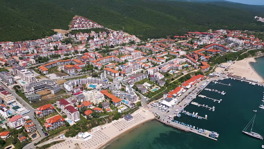 Aerial view of Sveti Vlas, a Bulgarian seaside resort town with a marina, beaches, red-roofed buildings, and green hills. Popular summer destination on the Black Sea coast