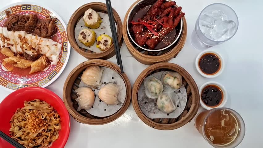 A flat lay view of a traditional Chinese food set with halal ingredients for shumai, chicken dumplings, spicy chicken feets, rice noodle rolls, shrimp hao kao, and beverages.