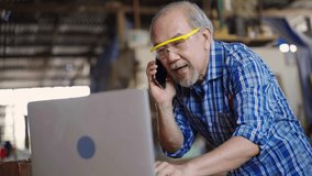 An elderly carpenter is multitasking in his wood workshop, checking customer orders on a laptop while speaking on the phone, reflecting small business operations and customer communication. - Powered by Shutterstock - Get 15% off with code: PIKWIZARD15
