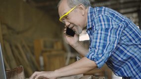 An elderly carpenter is multitasking in his wood workshop, checking customer orders on a laptop while speaking on the phone, reflecting small business operations and customer communication. - Powered by Shutterstock - Get 15% off with code: PIKWIZARD15
