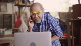An elderly carpenter is multitasking in his wood workshop, checking customer orders on a laptop while speaking on the phone, reflecting small business operations and customer communication. - Powered by Shutterstock - Get 15% off with code: PIKWIZARD15