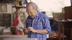 An elderly carpenter is multitasking in his wood workshop, checking customer orders on a laptop while speaking on the phone, reflecting small business operations and customer communication. - Powered by Shutterstock - Get 15% off with code: PIKWIZARD15
