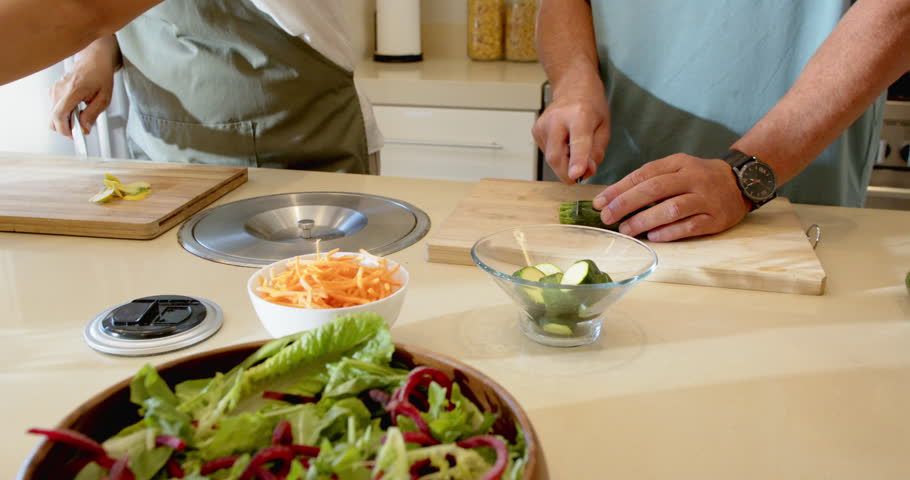 Senior diverse couple preparing fresh salad together in modern kitchen, enjoying cooking, at home. healthy eating, vegetables, culinary, lifestyle, togetherness, happiness