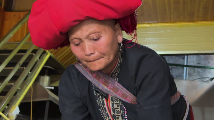 Elderly Black Dao woman forages herbs indoors, wearing traditional red headdress