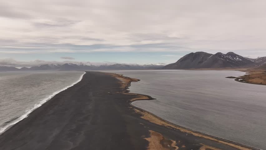 Aerial view of Vestrahorn mountain and the dramatic black sand beach at Stokksnes Peninsula, Iceland. Coastal beauty meets volcanic terrain under cloudy skies.