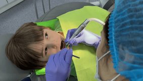 A doctor dentist in a medical mask and blue rubber gloves puts a seal on a little boy toddler. Dental treatment, examination with dental mirror, pediatric dentistry. Professional teeth cleaning - Powered by Shutterstock - Get 15% off with code: PIKWIZARD15