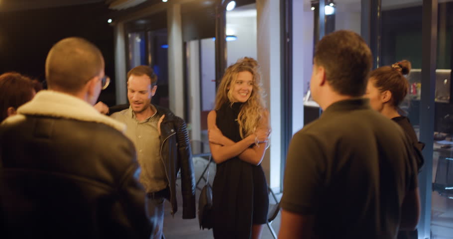 Friends enjoying drinks and conversation at a party. A man puts his jacket around a woman.