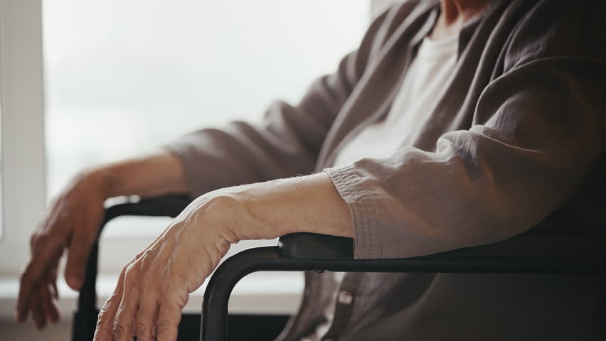 Nurse assisting elderly woman with disability to stand up from wheelchair