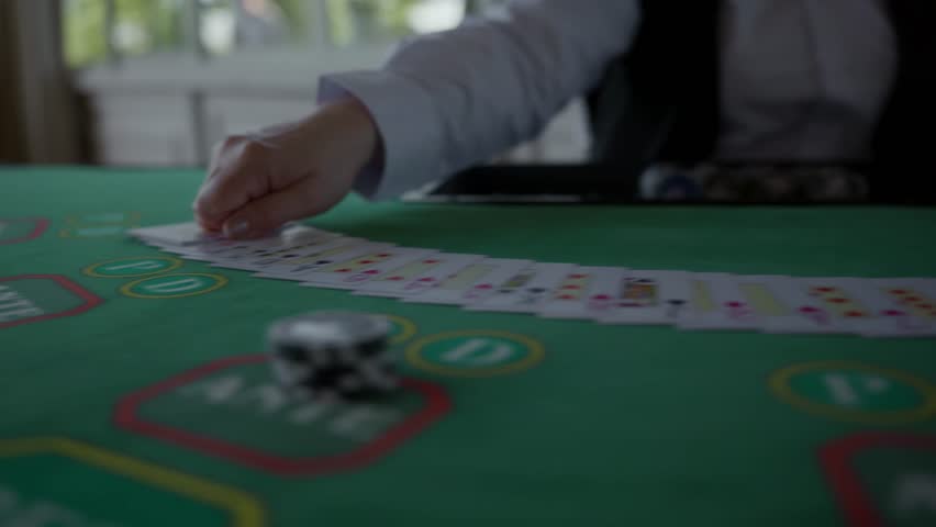 A professional croupier swiftly spreads a full deck of cards across the green table. Elegant hand movement highlights precision and skill in a casino setting. High quality 4k footage