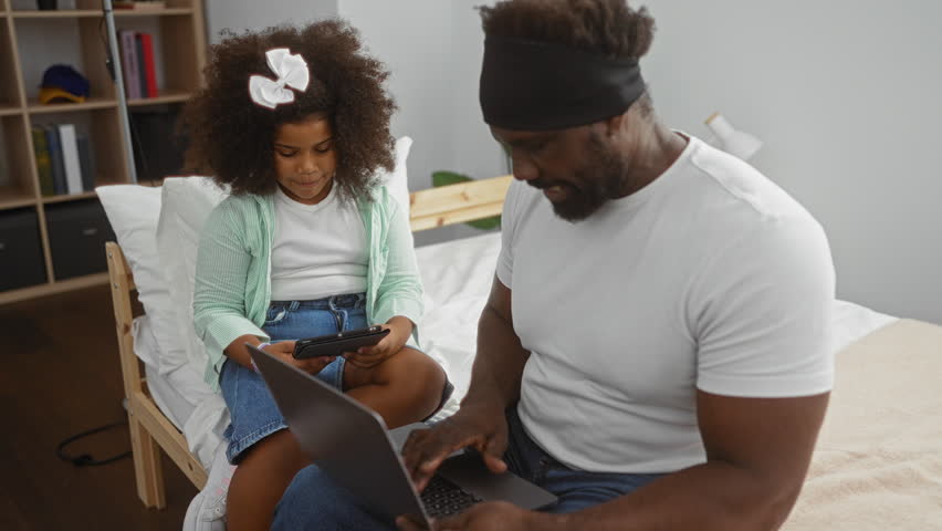 Father and daughter bonding in bedroom using tablet and laptop with love and joy, capturing family moments with happy expressions and togetherness indoors.