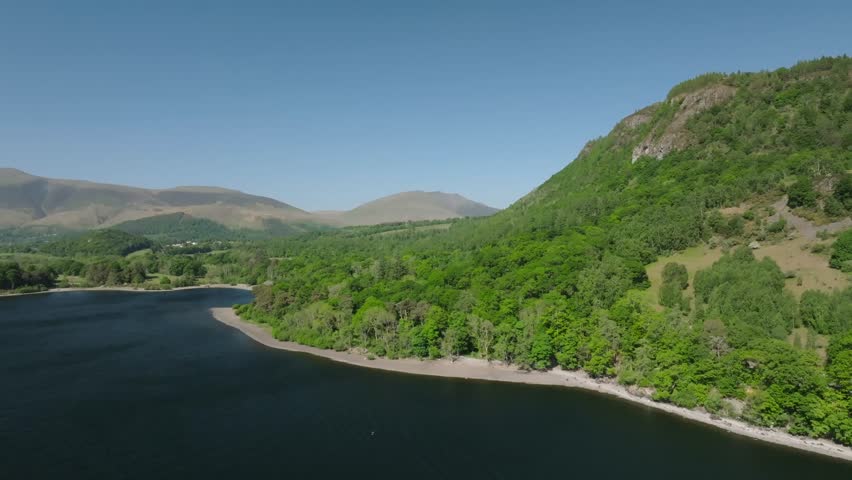 Rising above tree lined Cumbrian lake with views to distant mountains. Derwentwater, Lake District, Cumbria, UK.
