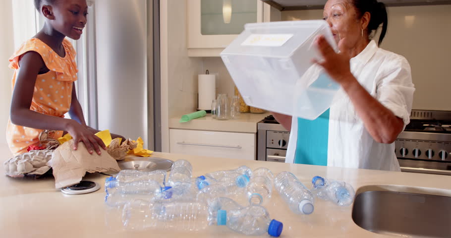 Grandmother and granddaughter sorting plastic bottles for recycling in kitchen, at home. sustainability, family, environment, waste management, conservation, eco-friendly