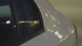 Close up side view of ash color car parked under streetlights at night, with vehicle window reflecting passing cars and blurred city lights creating glowing bokeh effect on body surface - Powered by Shutterstock - Get 15% off with code: PIKWIZARD15