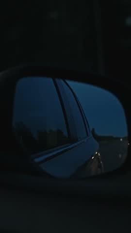VERTICAL VIDEO: View in the side rear view mirror of a car on the highway. Wanderlust concept. Night, evening, dusk. Road trip Europe Finland. Travel Background, vacation, weekend, travelling, freedom