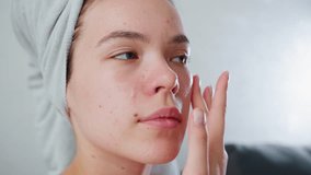 Closeup of young girl with towel wrapped around head applying skincare cream on face with finger, eyes closed, practicing facial self-care, treating acne-prone skin, focused on beauty - Powered by Shutterstock - Get 15% off with code: PIKWIZARD15