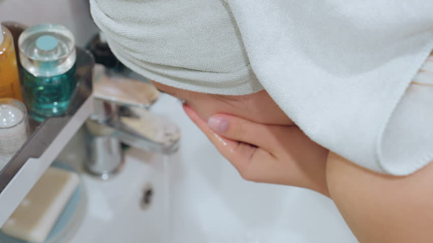 Close-up of lady raising her face to wash with tap water at sink, refreshing her skin, soft water flow emphasizes a gentle cleansing routine in a relaxing beauty care moment