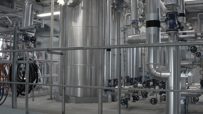 Descending drone shot revealing complex stainless steel piping, tanks, and industrial machinery inside modern factory, Castets, France