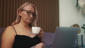 Middle-aged woman in glasses drinking tea and working on laptop in bed - Powered by Shutterstock - Get 15% off with code: PIKWIZARD15