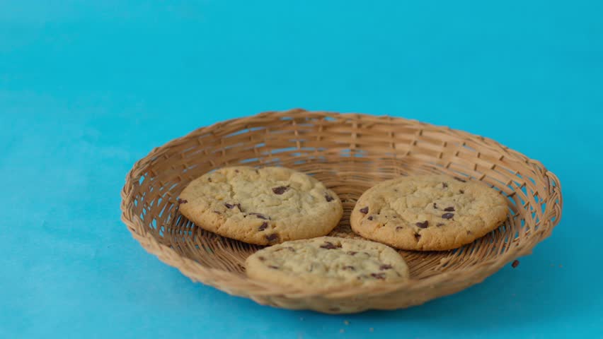 Three chocolate chip cookies in a basket on a blue background