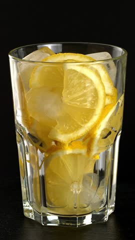 Glass of sparkling water with lemons and ice. Sparkling water is poured into a glass with ice and lemon. Close-up footage on the rotating table.