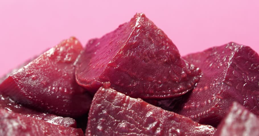 Red boiled beetroot cut into pieces rotates on pink background, close-up shot video