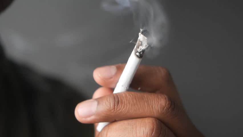 A closeup image of a hand firmly holding a smoky cigarette in detail