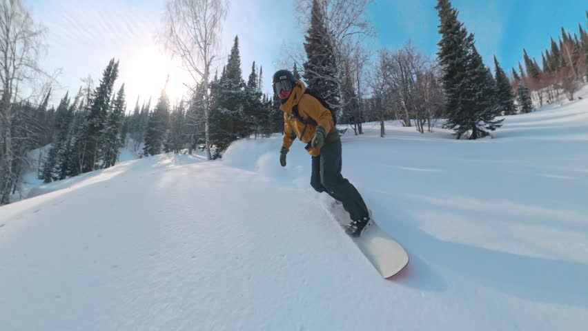 Professional snowboarder riding fast off piste in deep powder forest jumping over snow mounds spraying snow and carving between trees in extreme winter freeride mountain landscape