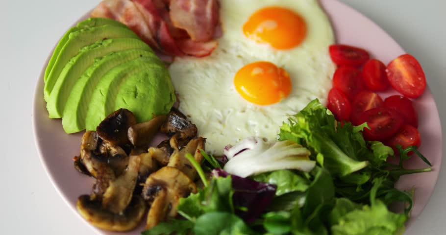 Mushrooms and avocado slices put on round plate creating breakfast atmosphere. Eggs and cherry tomatoes serve as elements of keto diet decorating dish
