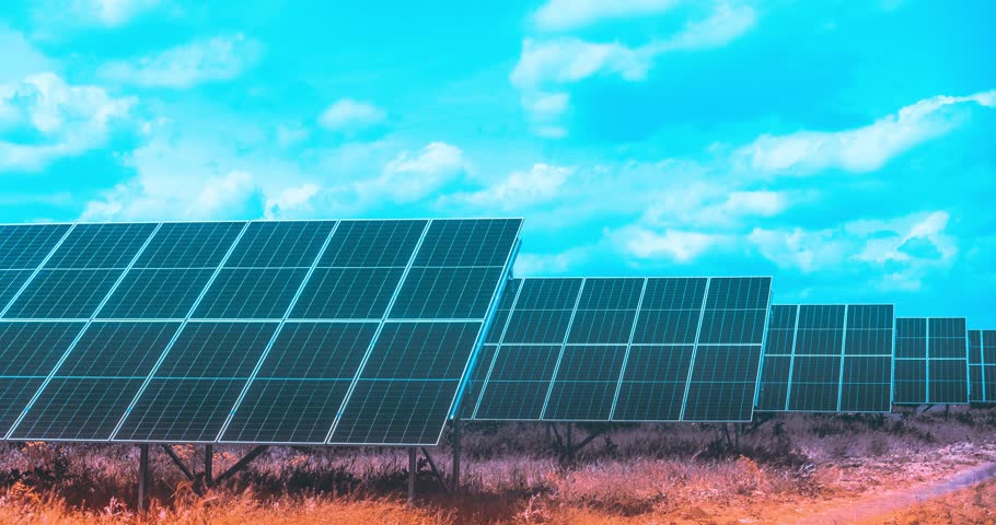 Time lapse showing a large solar panel field in open nature under a vivid blue sky with clouds, capturing renewable energy production in dynamic motion.