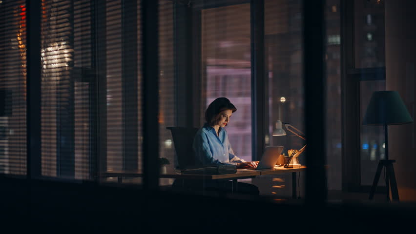 Night employee working on startup at dark corporate office. Hardworking businesswoman busy of overtime project looking laptop in lamp light. Elegant woman worker browse computer making deadline job.