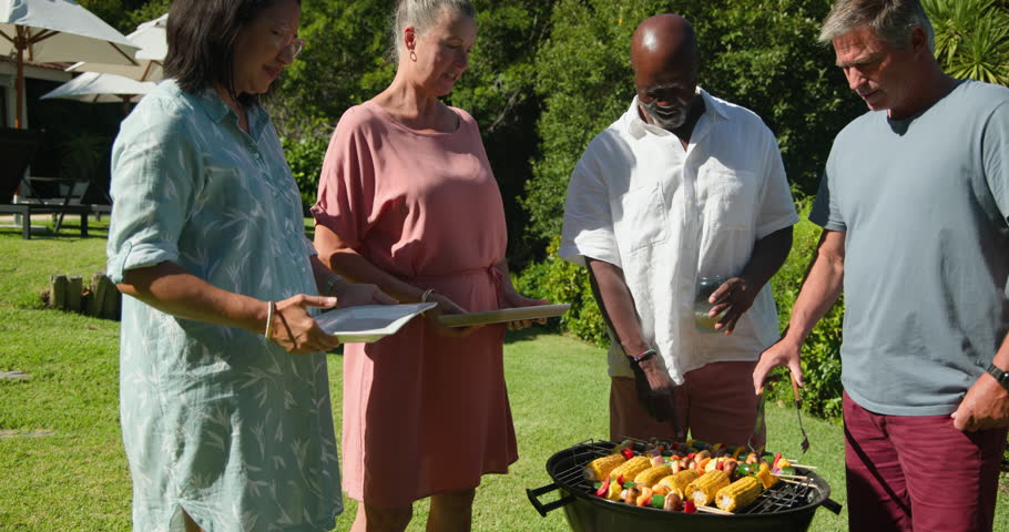 Grilling corn and vegetables in garden, diverse senior friends enjoying summer barbecue together. picnic, summertime, gathering, cooking, food preparation