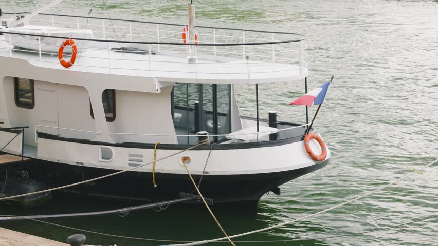 Moored modern white motorboat with a French flag on the bow of the boat on the right bank of the Seine River in Paris, France.