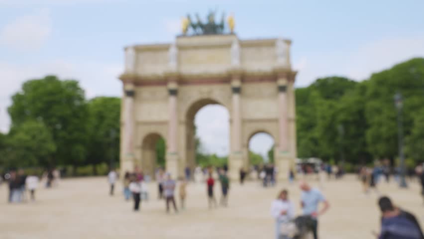 People stroll along the Place du Carrousel with a view of the Arc de Triomphe du Carrousel and the Jardin du Carrousel on a clear sunny spring day in Paris, France. Out of focus.