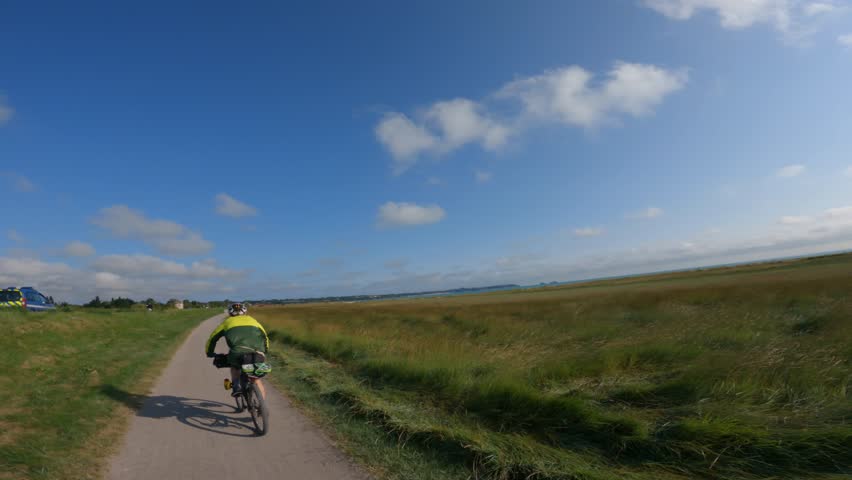 POV view of two cyclist rides on gravel bike path next to ocean in north of france region normandy towards Mont Saint-Michel. France cycling theme. Walking path and bike on beach of region Bretagne