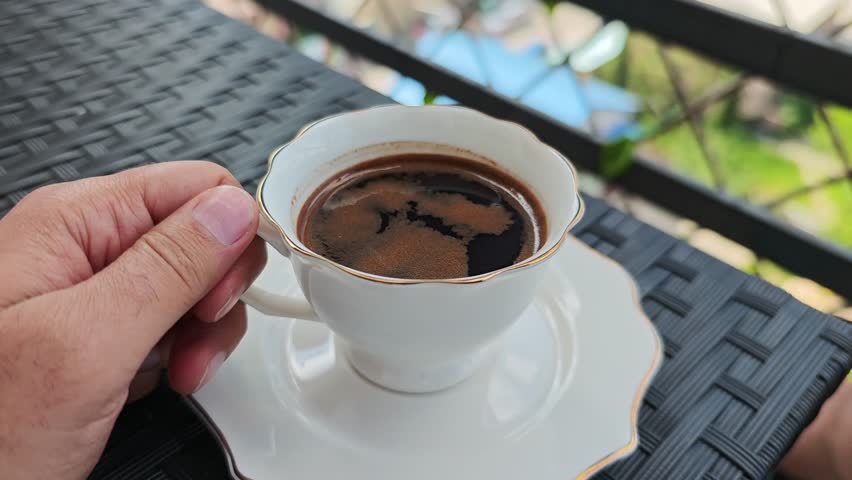 Hand lifting a cup of turkish coffee on a balcony table