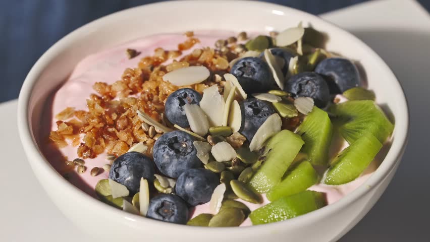 hand with a spoon takes yogurt with fresh berries and fruits and muesli from a bowl, food closeup, healthy breakfast