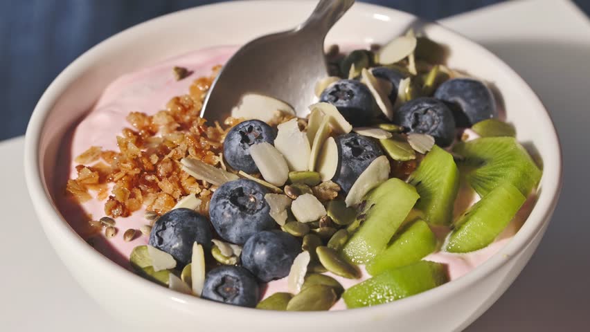 hand with a spoon takes yogurt with fresh berries and fruits and muesli from a bowl, food closeup, healthy breakfast