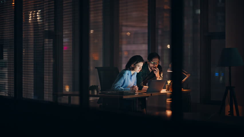 Business team frustrated bad news at laptop working overtime in dark office. Stressed colleagues worried project failure closing computer. Two upset managers feeling despair losing money late evening.