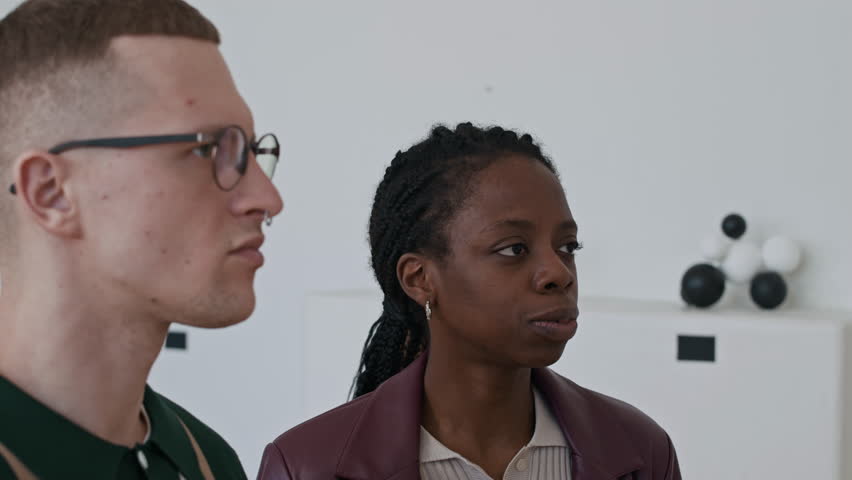 Side view closeup of trendy young man with nose piercing discussing art with friend while visiting modern art gallery exhibition
