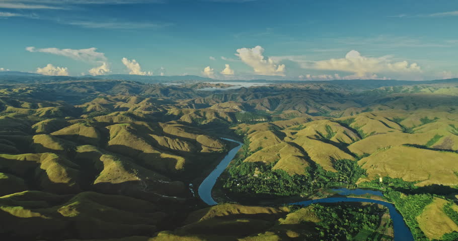 Aerial view of the Wanukaka River meandering through the undulating hills of Sumba Island, Indonesia, bathed in the golden light of sunrise, creating a breathtaking panorama of nature's beauty