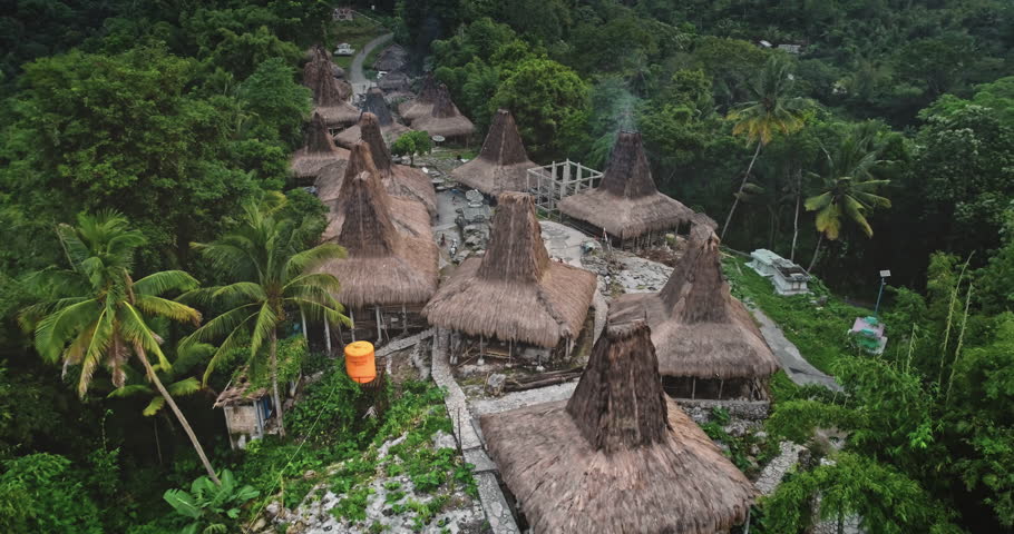 Aerial drone footage revealing traditional houses with conical roofs nestled in the lush tropical landscape of Sumba island, Indonesia, highlighting rich cultural heritage and unique architecture