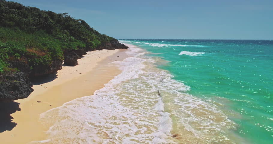 Breathtaking aerial view capturing turquoise ocean waves gently crashing on a pristine sandy beach, surrounded by lush green vegetation on Sumba Island, Indonesia