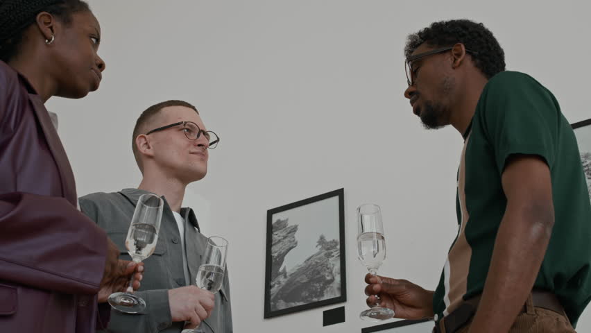 Low angle view at diverse group of smiling young people clinking champagne glasses and toasting during art gallery opening