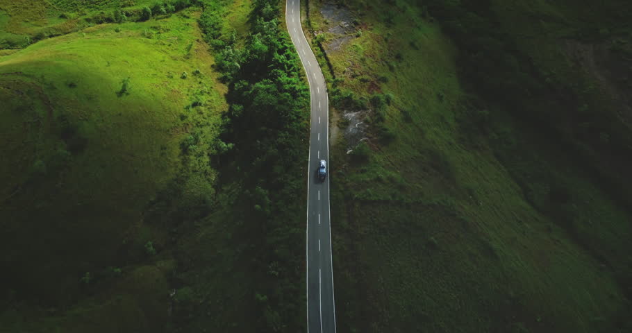 Aerial drone footage capturing a car driving along a winding road amidst the lush green hills of Sumba Island, Indonesia, showcasing the beauty of Wairinding Hill