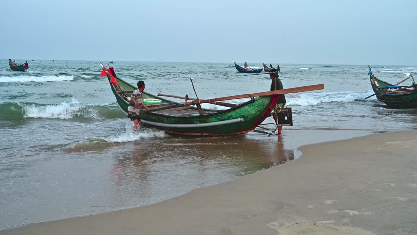 Asian Vietnamese male fishermen push traditional wooden boat on beach into sea in Vietnam in Asia. Tam Thanh, Quang Nam province, Vietnam - April 10, 2025