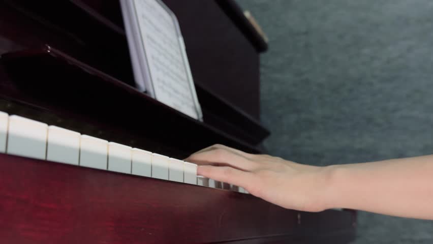 Hands Playing Piano: Training Notes with Emotion Concept. A hand is playing the keys of a wooden piano with sheet music placed on the stand.