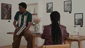 Shot of African American man as young artist showing artwork and prints to clients or managers during meeting in art gallery - Powered by Shutterstock - Get 15% off with code: PIKWIZARD15