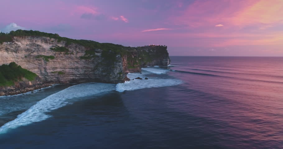 Uluwatu Temple standing on high cliff overlooking the beautiful Pantai Dreamland Beach with colorful sky during sunset in Bali, Indonesia, creating stunning scenery