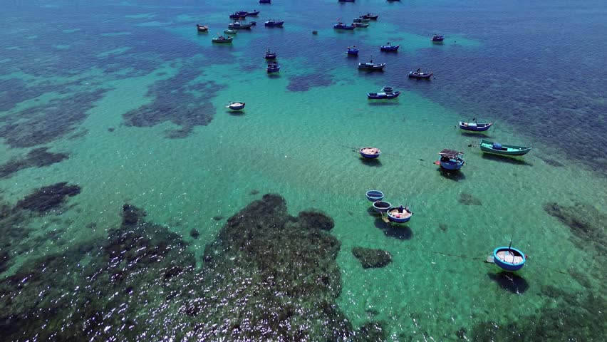 Aerial view of fishing village in Ninh Hải District, Ninh Thuận, captured moving forward with the camera tilted down to reveal the boats and coral patterns, Vietnam